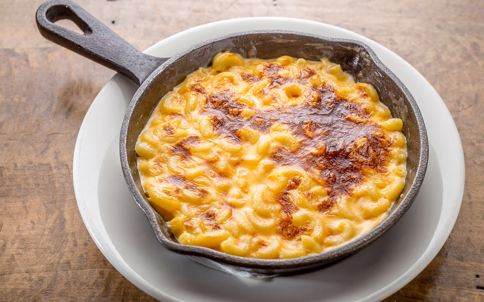 Baked macaroni and cheese with a golden brown crust in a cast iron skillet on a white plate.