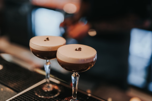 Two espresso martini cocktails with frothy tops and coffee beans garnish on a bar counter.